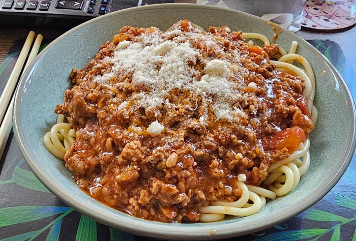 Plate of spaghetti with meat sauce and a sprinkle of cheese, chopsticks and a fork on the side