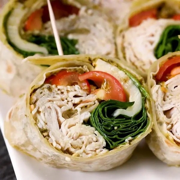 Close-up of sliced chicken wraps with fresh vegetables including lettuce, tomato, and cucumber, held together by toothpicks, served on a white plate