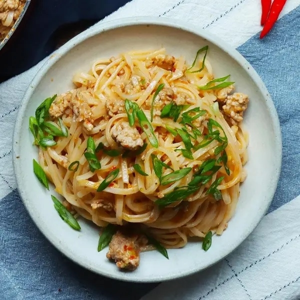 A bowl of freshly cooked noodles with minced meat and chopped green onions on top, served on a gray checkered tablecloth