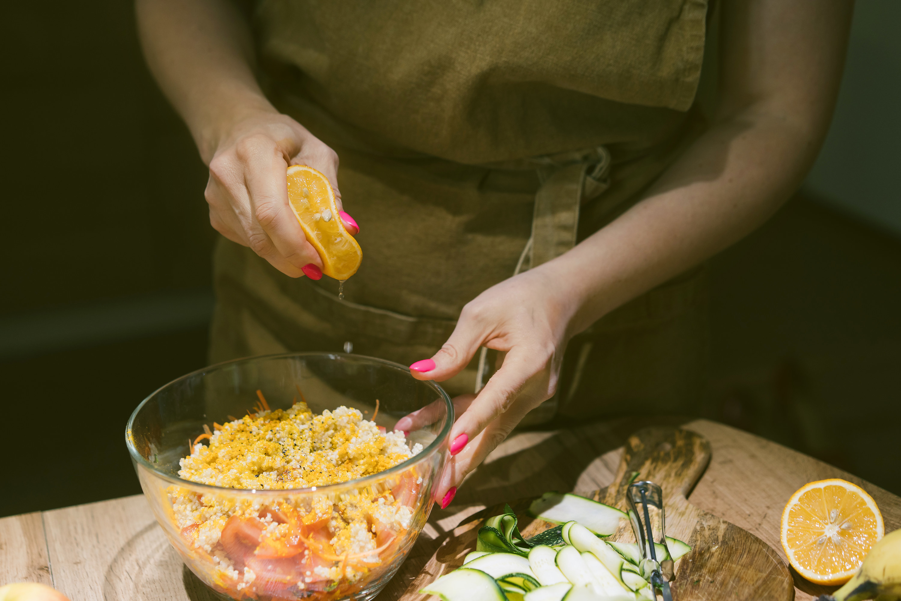 Hands squeezing lemon juice on a vegetarian salad of quinoa, tomato, carrot and spices