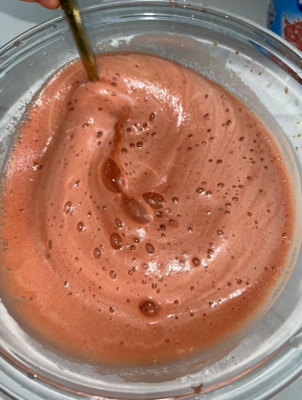 A bowl of a frothy liquid being mixed with a spoon